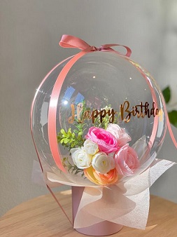 White rose Pink rose inside the clear happy birthday message on balloon encircled with pink ribbons and white net wrapping in a box